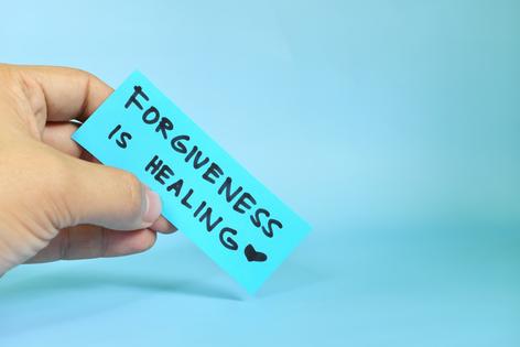 Forgiveness is healing concept. Hand holding a blue paper reminder message note. Getty Images