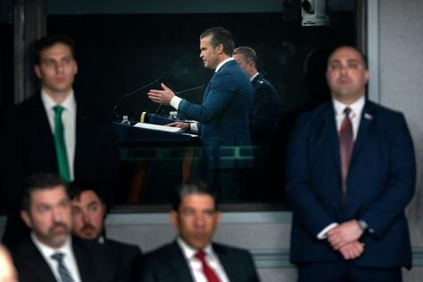 Staff members watch as Defense Secretary Pete Hegseth speaks during a press briefing at the Pentagon on March 2, 2026.  AP Photo/Mark Schiefelbein