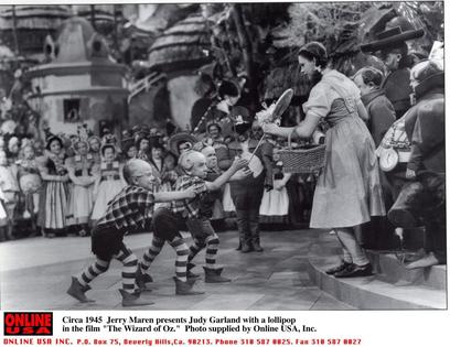 1939: Jerry Maren, playing a Lollipop Guild Member, presents Judy Garland with a lollipop in the film 