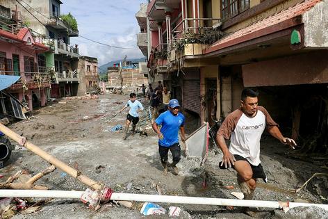 Residents run through a mud-covered street, where the debris shows the flood reached well into the second flood of homes, on Aug. 26, 2026. Hundreds of people are missing on the Nepal-Tibet border after the flood swept away homes and cut off villages.
              Prabin Ranabhat/AFP via Getty Images