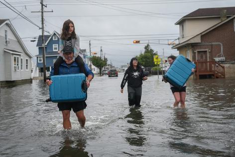 A family carries their belongings through the water of a flooded road during a nor'easter storm on Sept. 26, 2026, in Point Pleasant, N.J., where a voluntary evacuation had been issued.
              Ryan Murphy/Getty Images