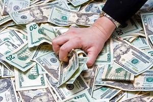 Greed. Woman's hand grabbing money from a huge pile of dollars. Dreamstime/TCA