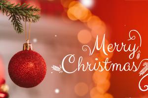 A shiny red ornament hangs from a green pine branch with a blurred glowing background. Getty Images