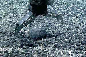 A metal claw reaches for an iron and manganese nodule on the seabed for testing. USGS Pacific Coastal and Marine Science Center